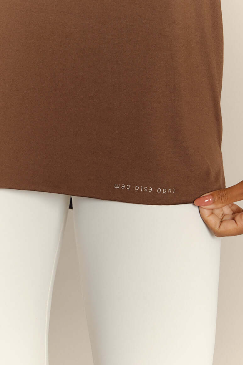 Brown oversized Regata Over Café Coragem top with white text, paired with white leggings, showing fabric texture and fit.